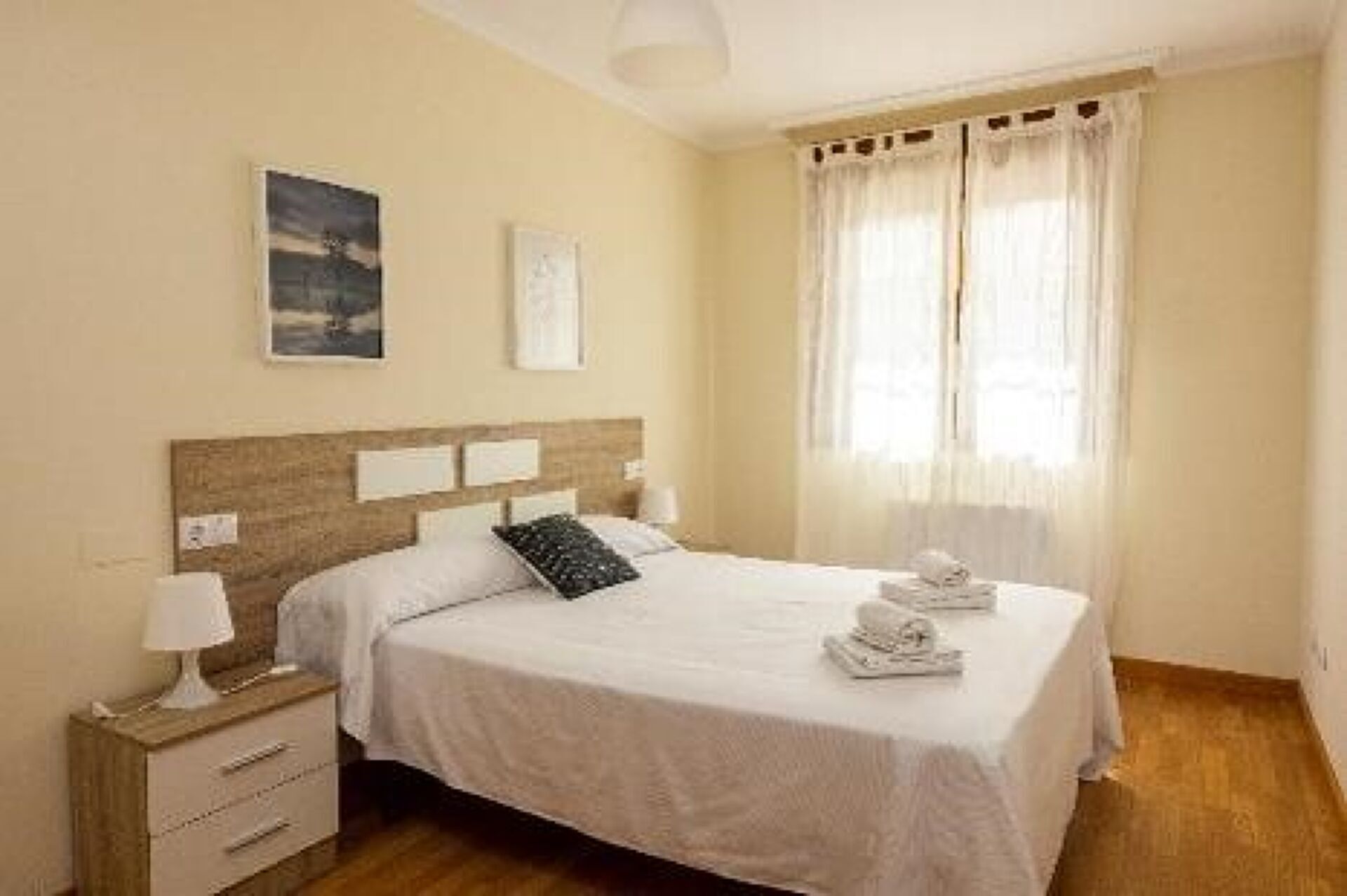 A neatly arranged bedroom with a bed, bedside tables, and a window with curtains.