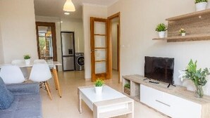 Ein modernes Wohnzimmer mit Sofa, Couchtisch, Fernseher und einer Küche im Hintergrund.