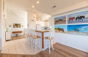 A modern kitchen with white cabinets, a wooden dining table with four chairs, and a wall adorned with horse-themed artwork.