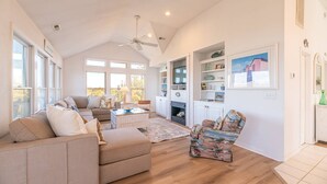 A spacious living room with a high ceiling, a fireplace, and a large window. - The BARNacle - Corolla, Ocean Sands, 5 Min. Walk to Beach, Pool, Hot Tub, Pets OK, Flex Stays (Corolla)