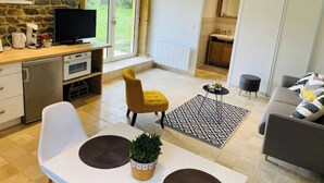 Una sala moderna con pared de piedra, televisor, comedor con mesa y sillas, sofá y cocina al fondo.