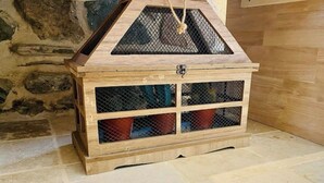 Un cofre de madera con tapa articulada y parte superior de malla, sobre un suelo de piedra.