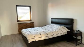Une chambre à coucher comprenant un lit, une table de chevet, une commode et une fenêtre avec des stores.