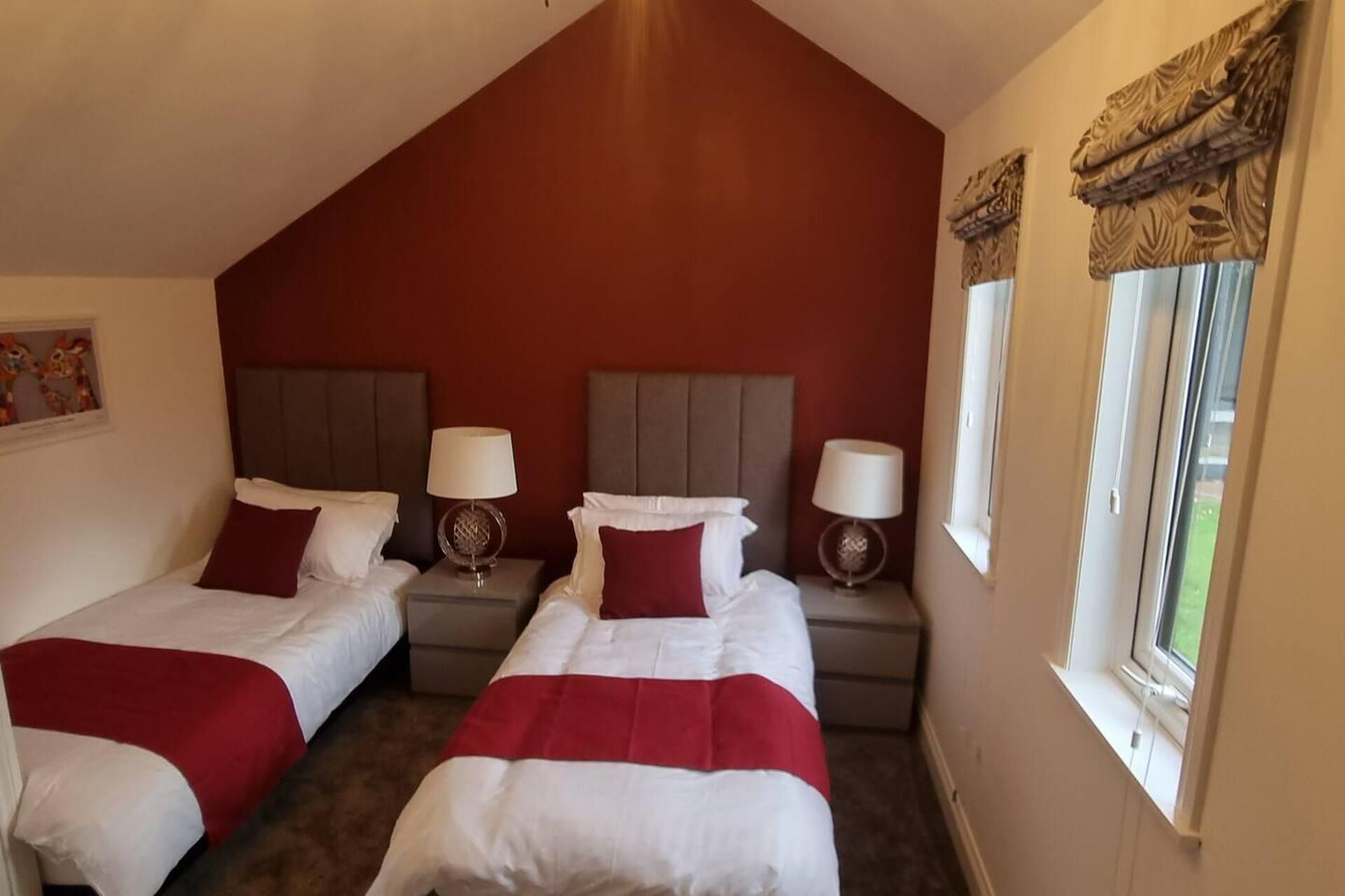 A hotel room with two beds, each with a red and white bedspread, and a large window with curtains.