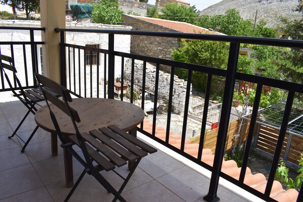 A balcony with a table and chairs, overlooking a courtyard with stone walls and terracotta planters.