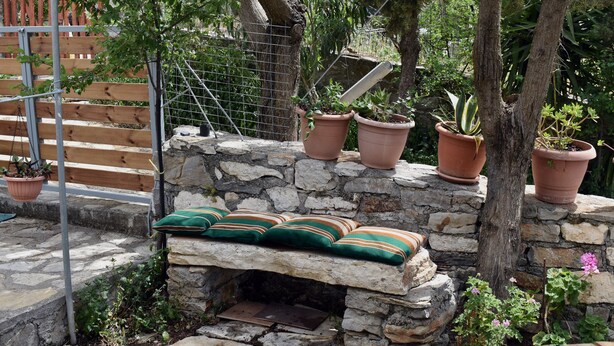 A stone bench with cushions, surrounded by potted plants and a rustic stone wall. - Ethia 2floor Mountain View Cottage Garden Wifi ac (Archanes-Asterousia)