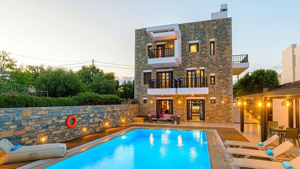 Un edificio moderno de dos pisos con piscina, mobiliario exterior y fachada de piedra.