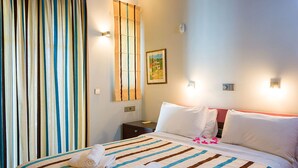 Una habitación de hotel con cama, mesita de noche, un cuadro en la pared y una cortina.
