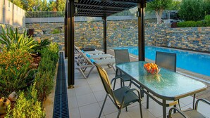 Un espacio al aire libre techado con piscina, sillones de descanso y una mesa con un frutero.