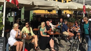 Un grupo de personas sentadas en mesas al aire libre frente a un edificio con un letrero que dice "NYHAVN 17".