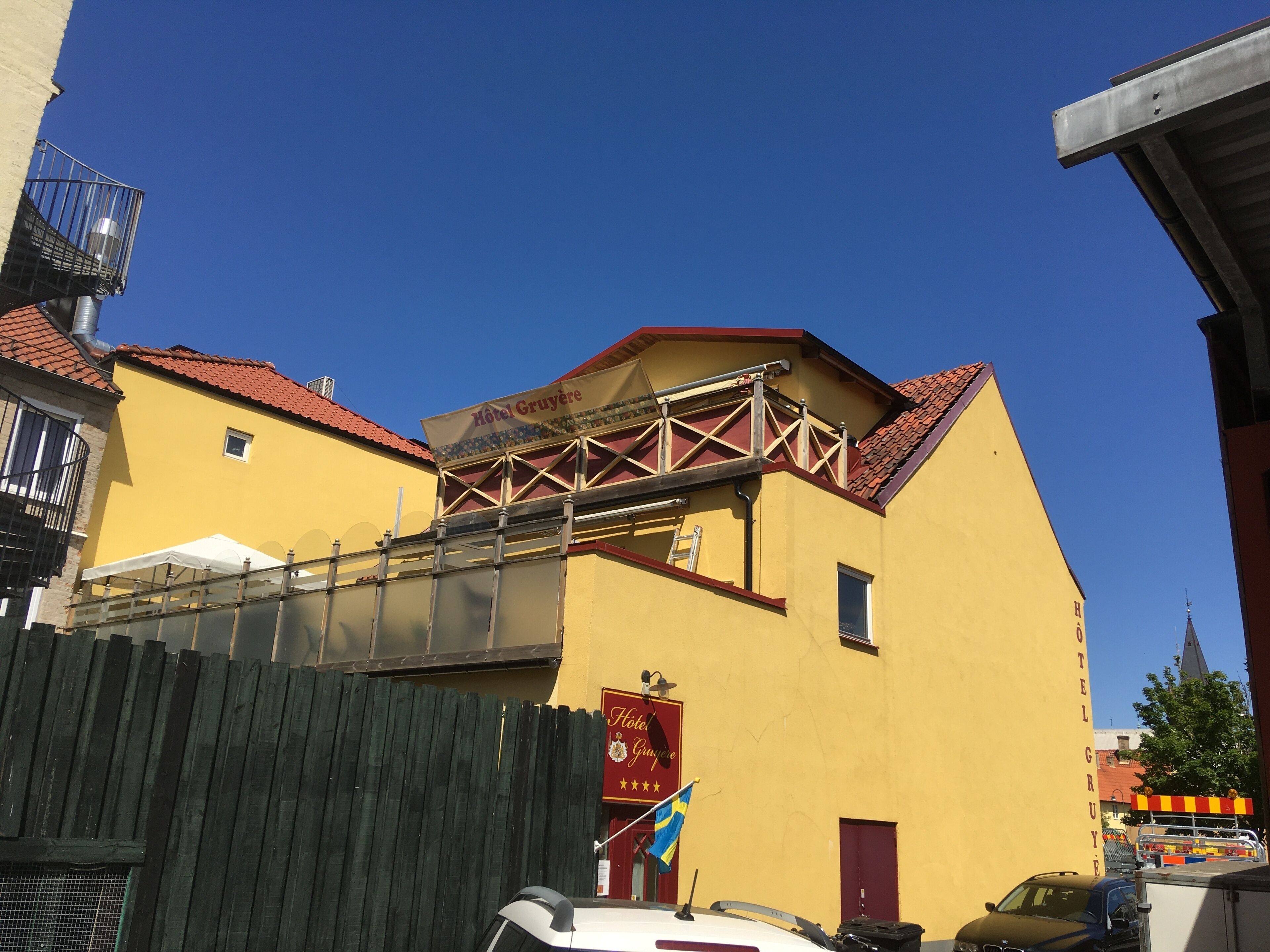 A yellow building with a red roof, a sign reading "Hotel Gruyère," and a flag.