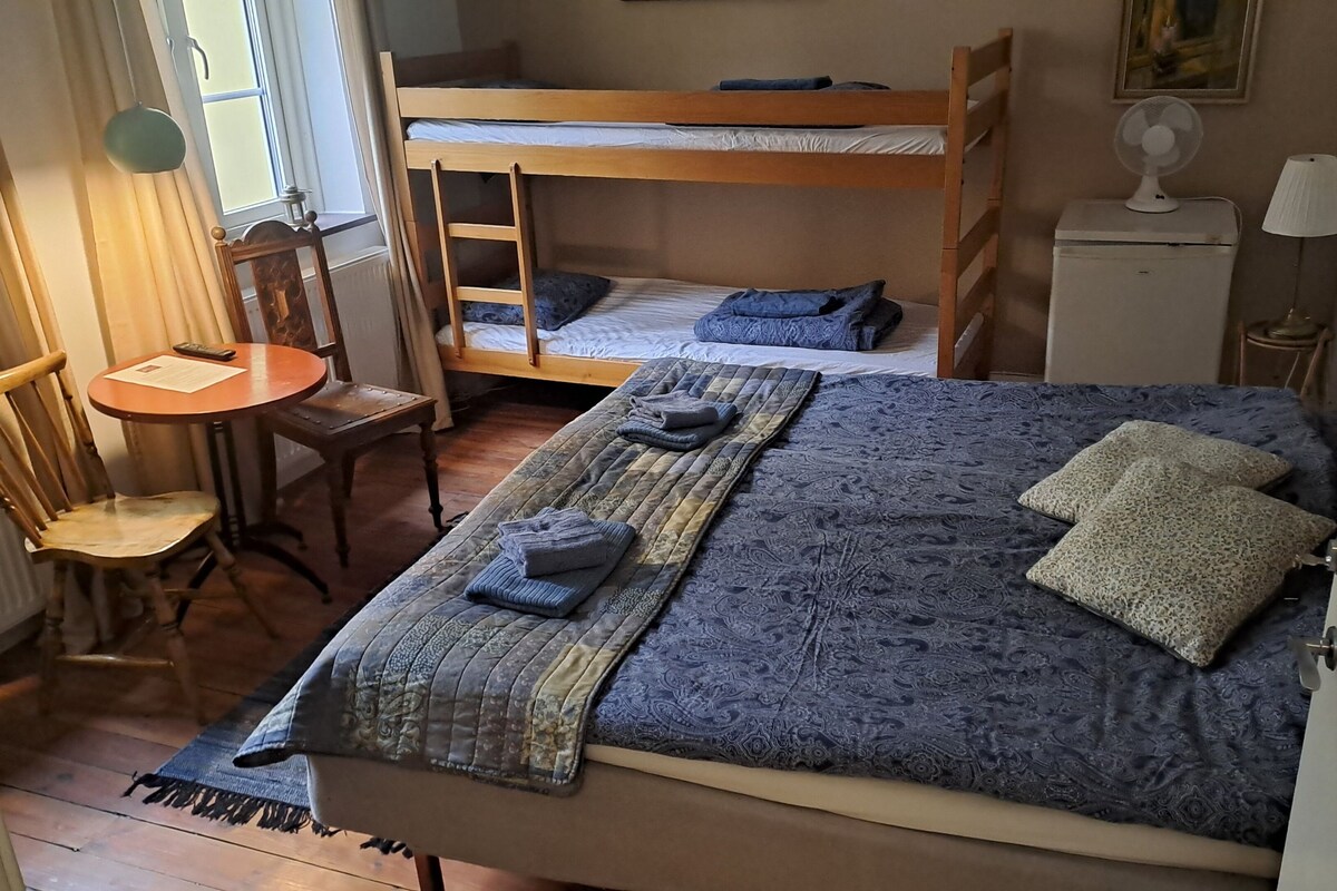 A bedroom with a bunk bed, a desk with a chair, a lamp, and a fan.