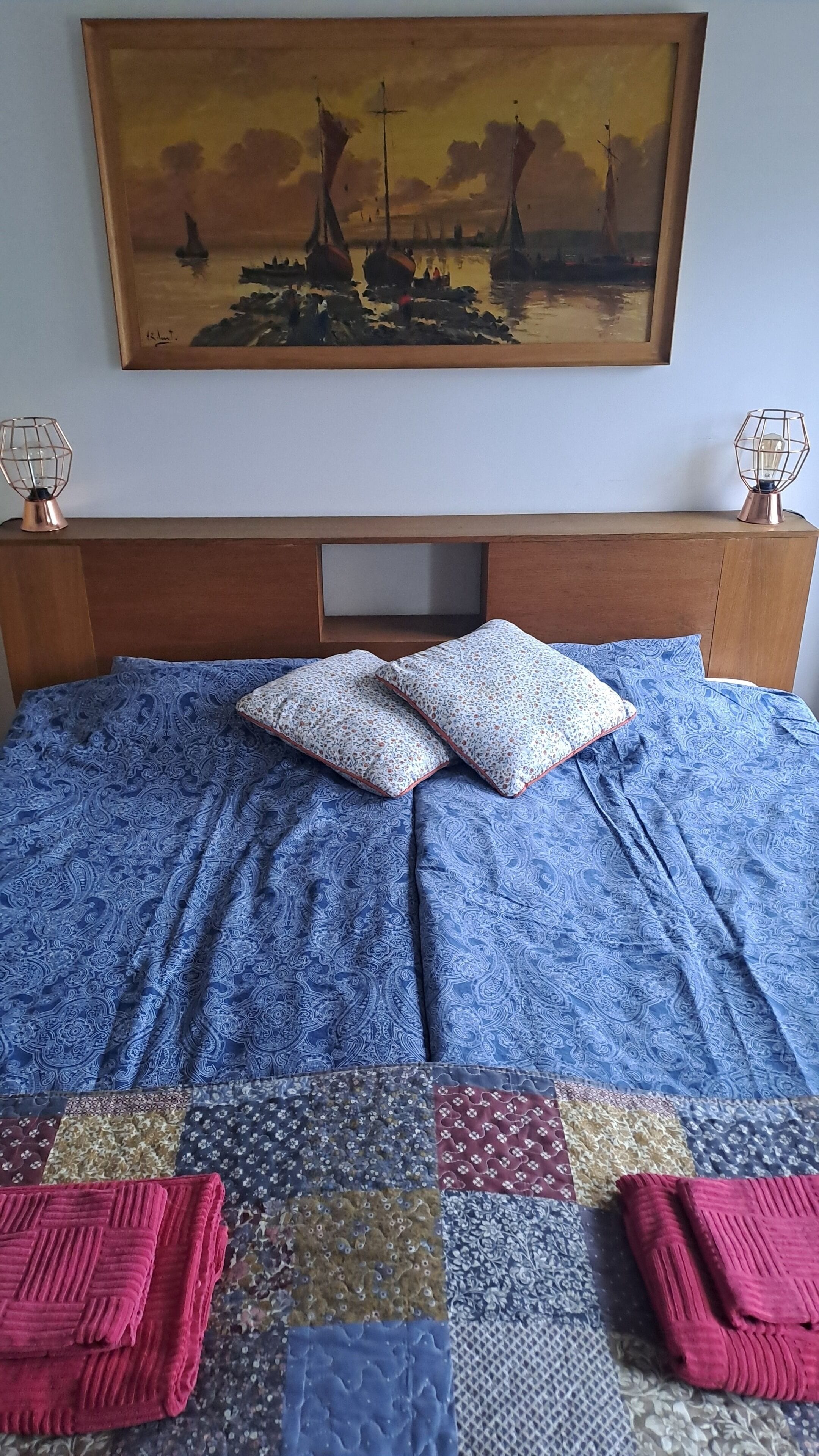 Una cama con colcha azul estampada, dos almohadas y una colcha con diversos diseños.