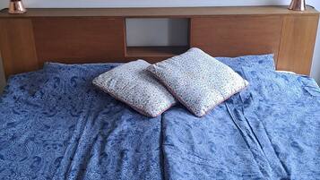 Una cama con colcha azul estampada, dos almohadas y una colcha con diversos diseños.