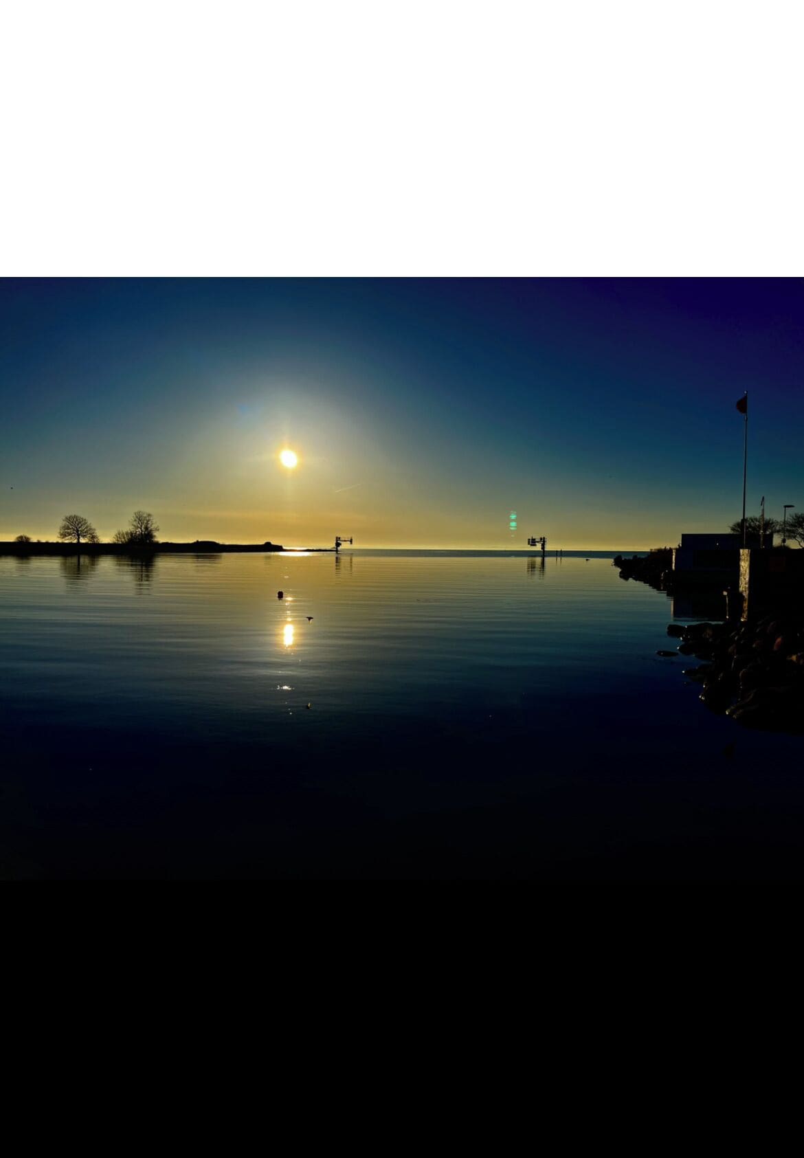 A calm body of water reflecting the sun, with a clear sky and distant horizon.