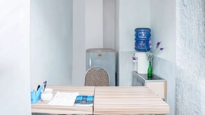 Een kleine, verzorgde kamer met een houten tafel, een stoel, een waterdispenser en een klein kastje.