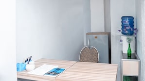 Een kleine, verzorgde kamer met een houten tafel, een gestreept stoel, een koelkast en een waterdispenser.