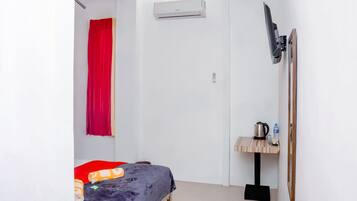 A small, compact room with a bed, a small table with a kettle, and a red curtain.