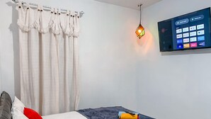 Een kamer met een bed, een aan de muur bevestigde televisie en een hanglamp.