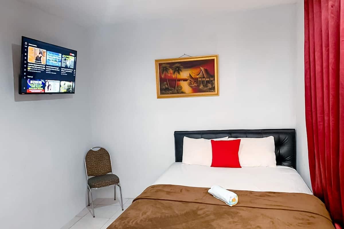 A hotel room with a bed, a chair, a TV mounted on the wall, and a painting above the bed.
