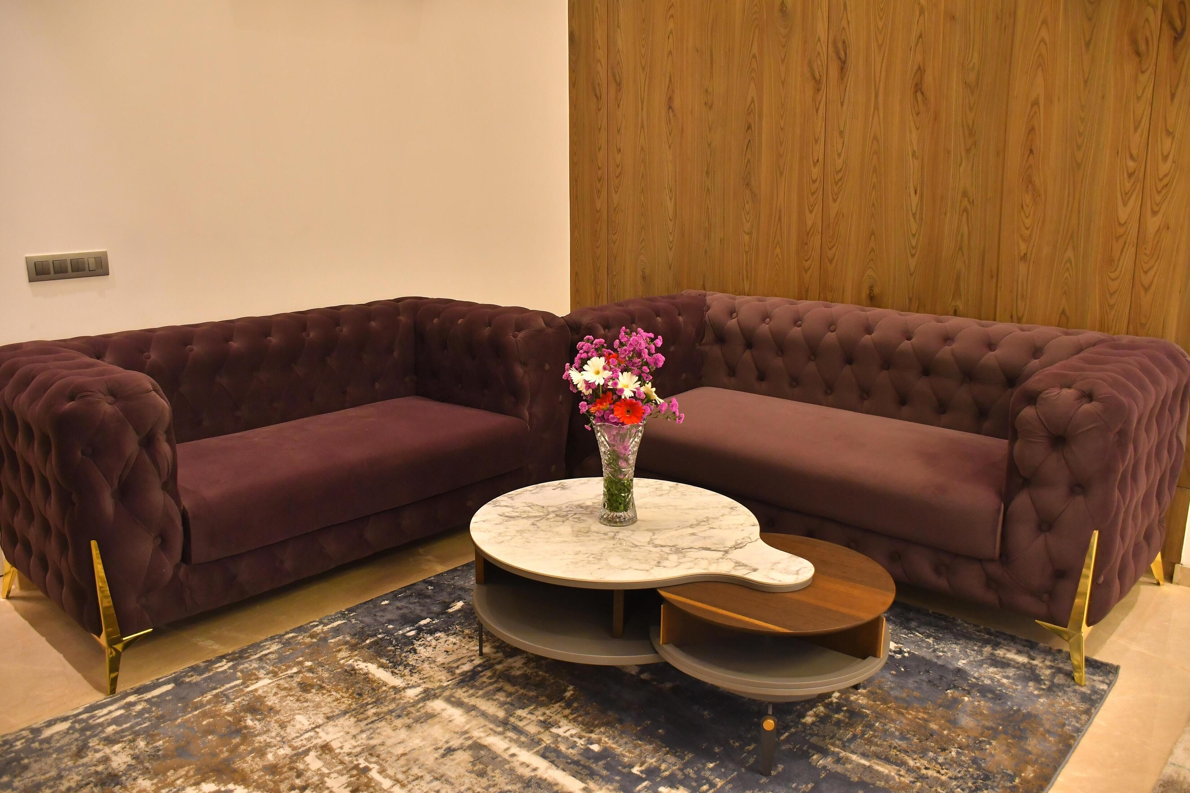 A modern living room with a plush purple sectional sofa, a marble coffee table with a vase of flowers, and a unique rug with a distressed look.