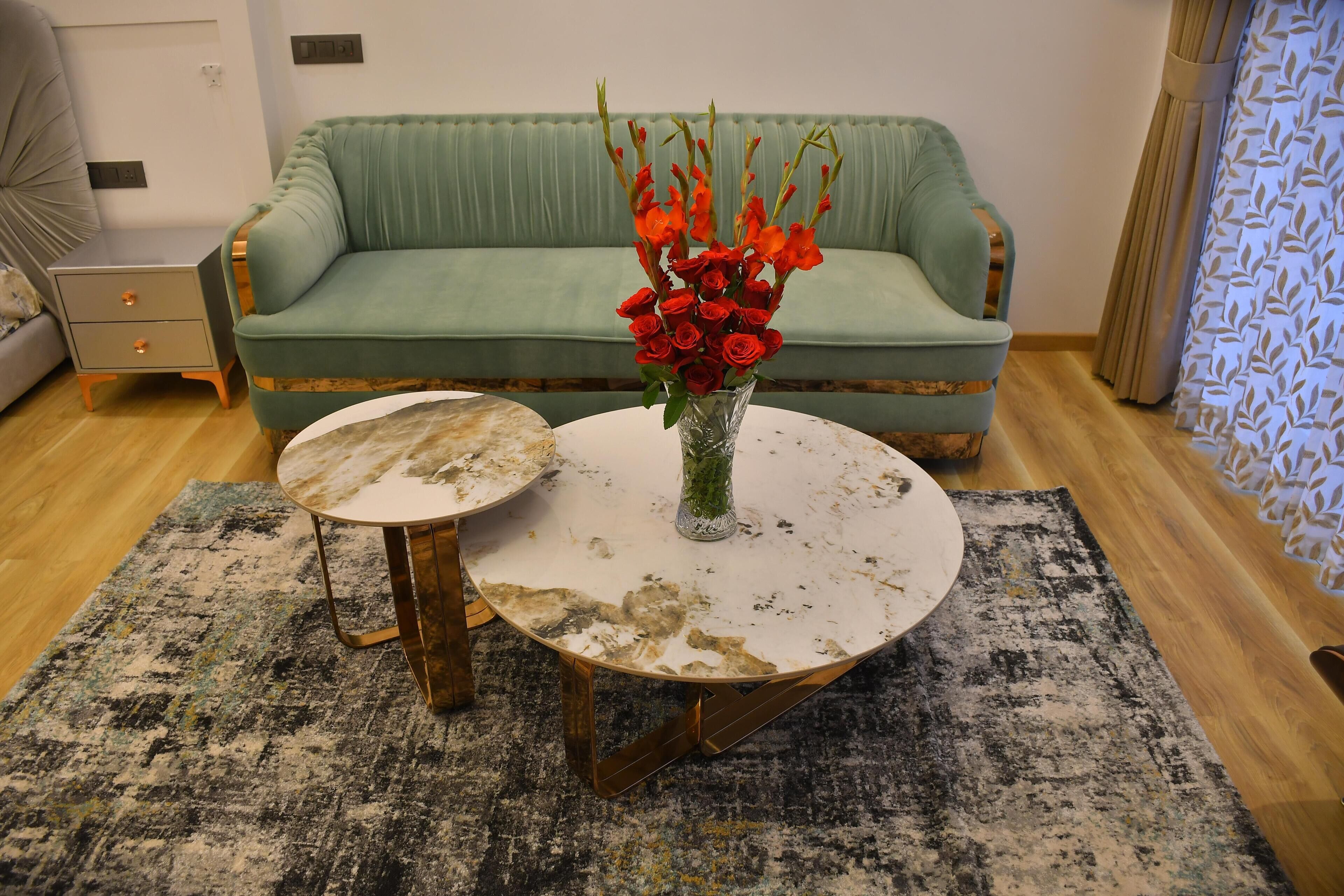 A room with a green sofa, a small table with a vase of red flowers, and a patterned rug.