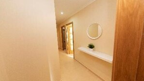 A hallway with a wooden door frame, a white wall-mounted shelf with a small plant, and a round mirror. - MAR DE VICEDO - PENTHOUSE 2 BEDROOMS WITH TERRACE (O Vicedo)