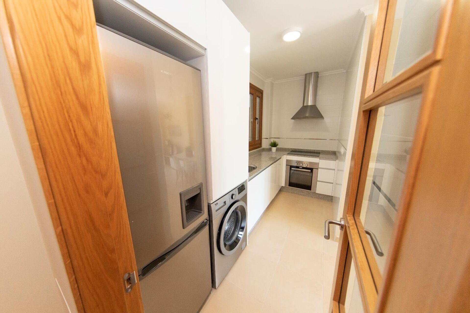 Una cocina funcional con lavadora, horno integrado y refrigerador de acero inoxidable.