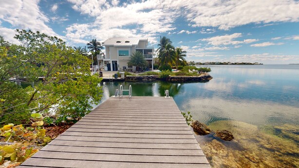 A wooden dock leading to a house with a pool and a view of a calm lake. - Sea La Vie - Your Oceanfront Escape - 3BD/3Bath - Cudjoe Key (Cudjoe Key)