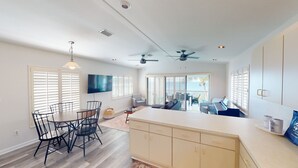 A spacious living area with a dining table, chairs, a sofa, and a TV. There are ceiling fans and a large window with blinds. - Sea La Vie - Your Oceanfront Escape - 3BD/3Bath - Cudjoe Key (Cudjoe Key)