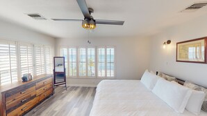 A bedroom with a bed, wooden dresser, ceiling fan, and large windows with blinds. - Sea La Vie - Your Oceanfront Escape - 3BD/3Bath - Cudjoe Key (Cudjoe Key)