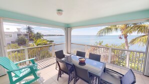 A balcony with a table and chairs, overlooking a body of water and palm trees. - Sea La Vie - Your Oceanfront Escape - 3BD/3Bath - Cudjoe Key (Cudjoe Key)