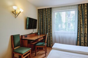 Een hotelkamer met een houten bureau, twee stoelen, een bed, een televisie en gordijnen met een patroon.