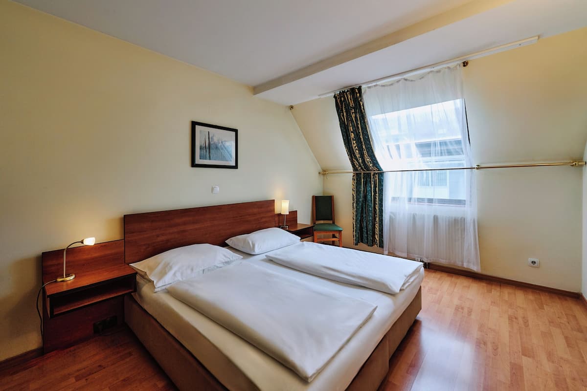 A bedroom with a wooden bed, two bedside tables with lamps, a chair, and a window with curtains.
