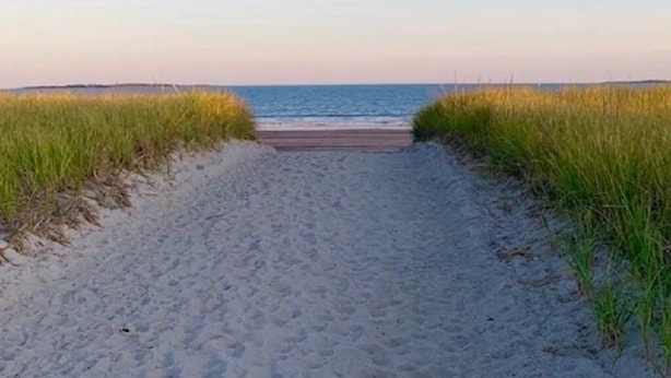 A sandy beach path leading to the ocean, flanked by grassy dunes.