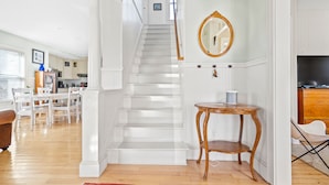 A staircase leading to a second floor, a round wooden table, and a television on a wooden cabinet.