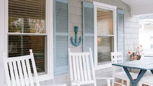 A covered patio area with white wooden chairs and a table, featuring blue shutters and a decorative anchor on the wall.