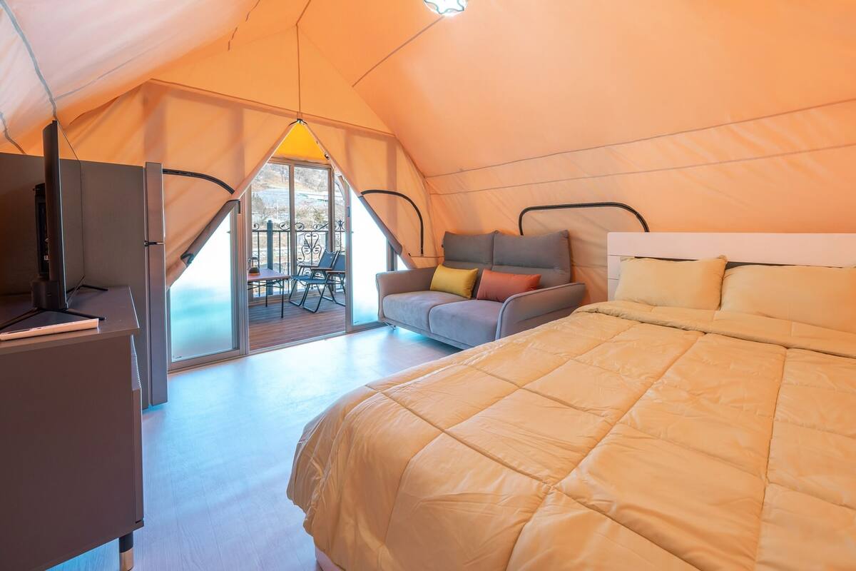 Un dormitorio tipo tienda de campaña con cama, sofá y escritorio con una computadora portátil.