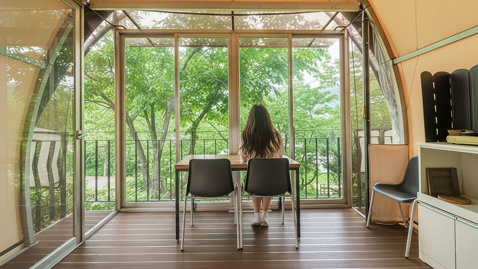 A tented room with a table and chairs, large windows, and a view of trees.