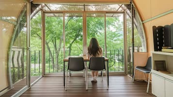A tented room with a table and chairs, large windows, and a view of trees.