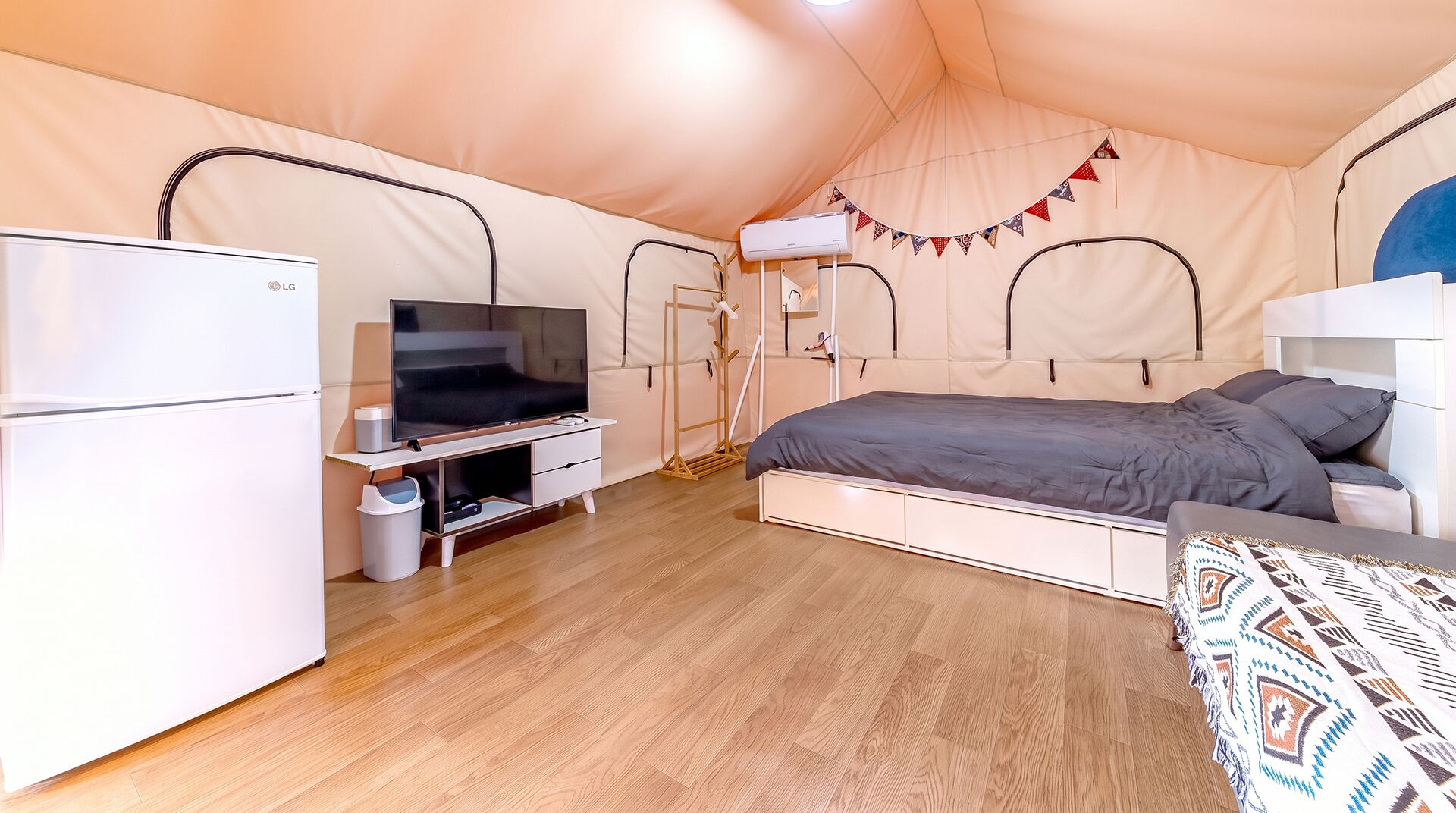 A tent-style room with a bed, a TV, a fridge, and a heater.