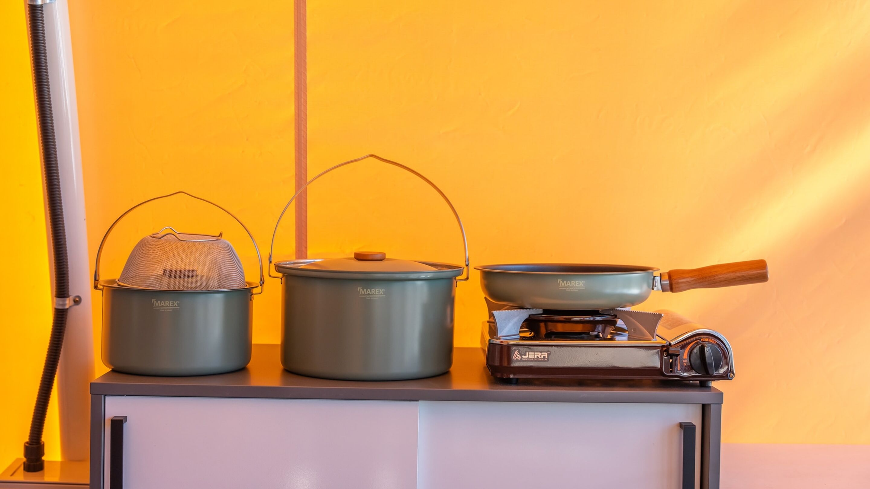 A kitchen setup with two pots, a strainer, and a frying pan on a stove.