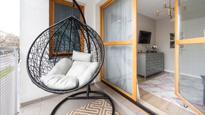 Un balcón con una silla colgante, una puerta corredera de cristal, un televisor y un mueble bajo.