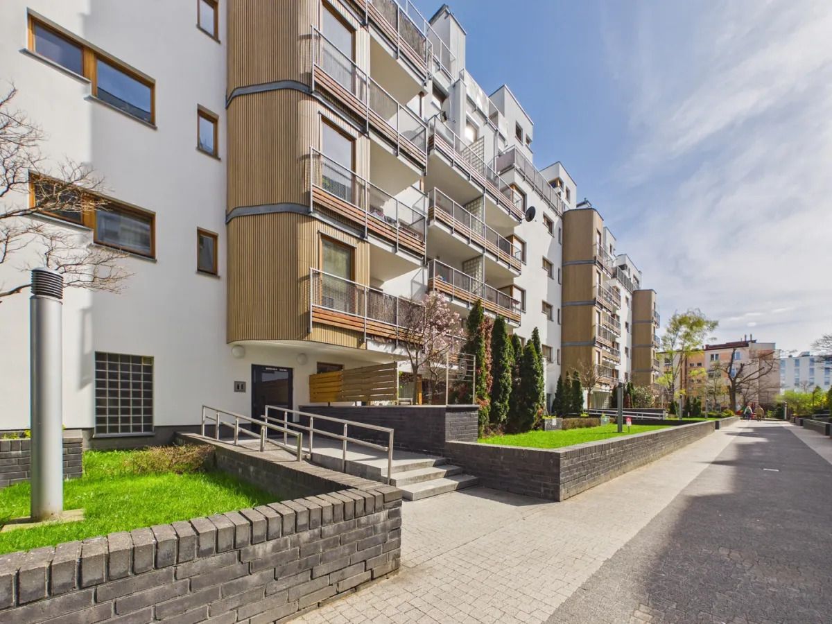 Un edifici d'apartaments modern amb balcons, un passeig pavimentat i una petita zona de jardí.