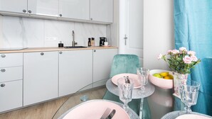 Una cocina moderna con armarios blancos, encimera de madera y una zona de comedor con vajilla rosa y verde.