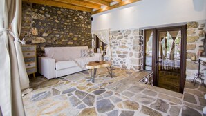 Une pièce chaleureuse avec un mur en pierre, des poutres apparentes en bois au plafond, un canapé blanc et une petite table ronde.