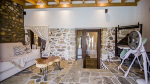 Un salon chaleureux avec un mur en pierre, un plafond en bois, un canapé blanc, une table basse en bois et un ventilateur.