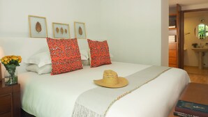 A neatly made bed with a white bedspread, two red patterned pillows, and a straw hat on the bed. There is a small vase with yellow flowers on the nightstand. - Comfort Reforma By The Local Way (Mexico City)