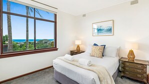 A bedroom with a large window, a bed, two bedside tables, and a wall-mounted artwork. - Welcome to The Lookout, a beautiful 4 bedroom house with stunning ocean views. (Coffs Harbour)