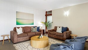 A living room with two brown sofas, a round coffee table, and a large abstract painting on the wall. - Welcome to The Lookout, a beautiful 4 bedroom house with stunning ocean views. (Coffs Harbour)